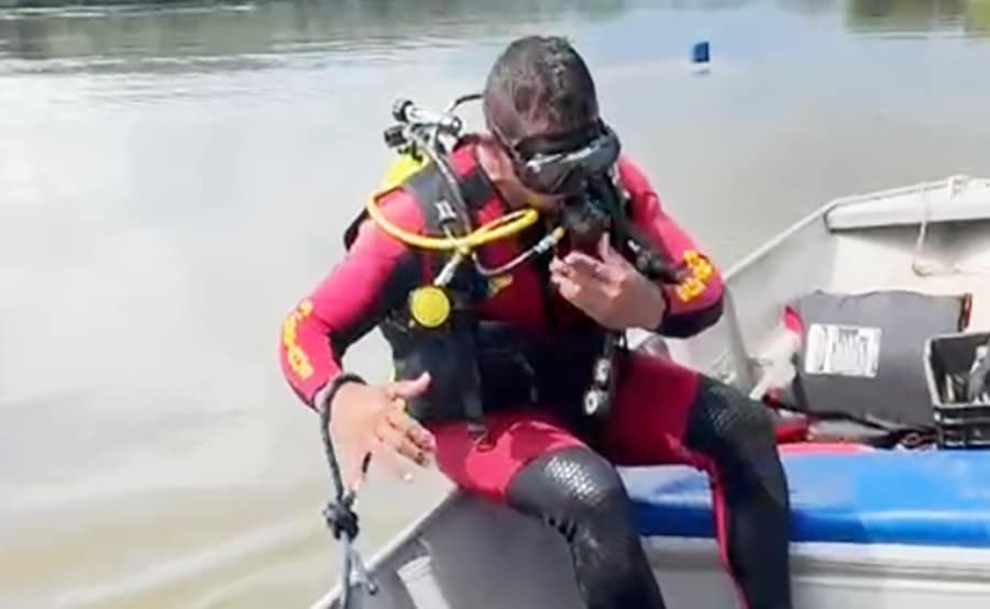 Mergulhador do Corpo de Bombeiros sentado na lateral de um barco durante busca em represa