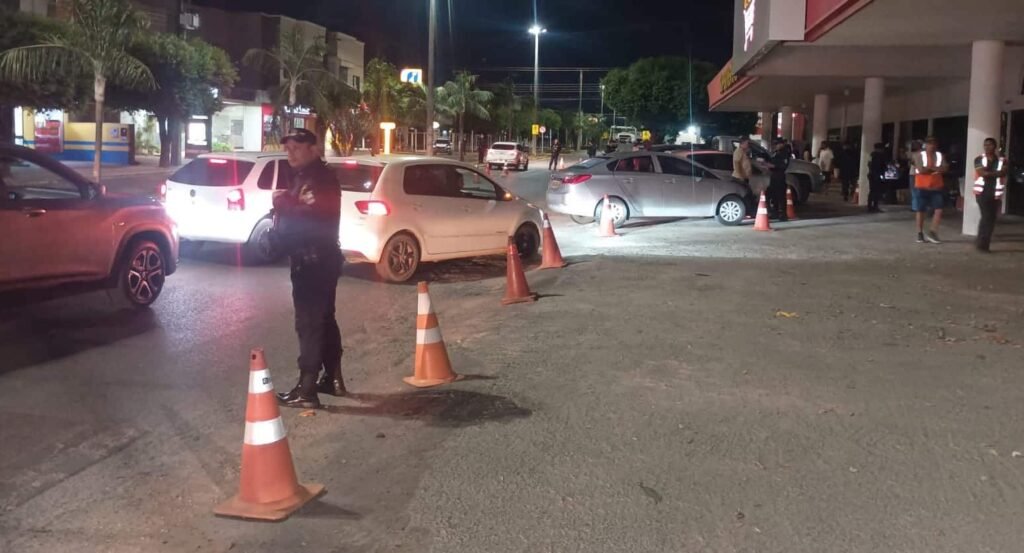 Policiais e veículos em ponto de fiscalização de trânsito à noite, com cones de sinalização