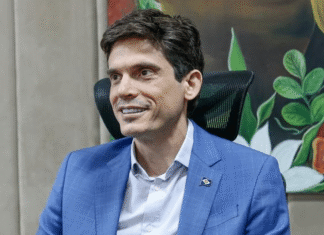 Eduardo Manciolli, de terno azul, sorri sentado em escritório