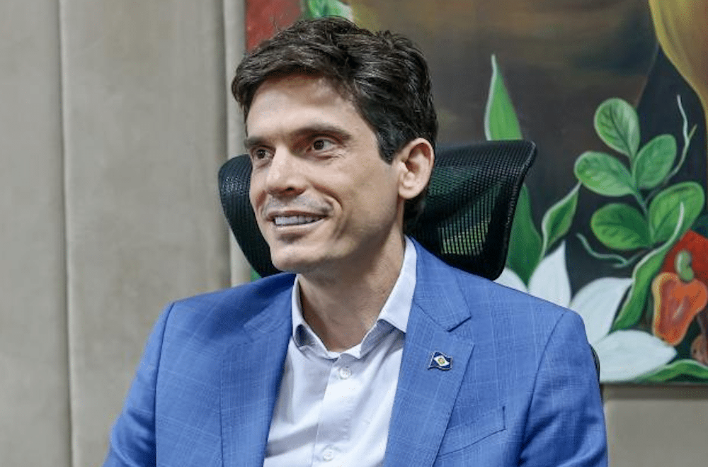 Eduardo Manciolli, de terno azul, sorri sentado em escritório
