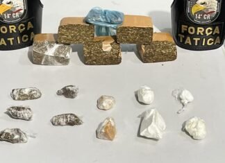 Tabletes de maconha e porções de cocaína sobre uma mesa, ao lado de dois coletes da Força Tática