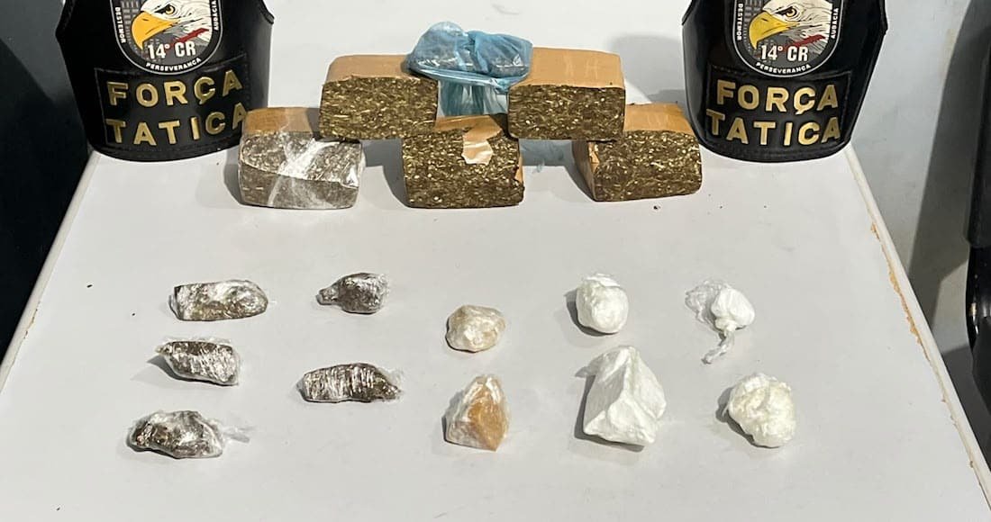 Tabletes de maconha e porções de cocaína sobre uma mesa, ao lado de dois coletes da Força Tática