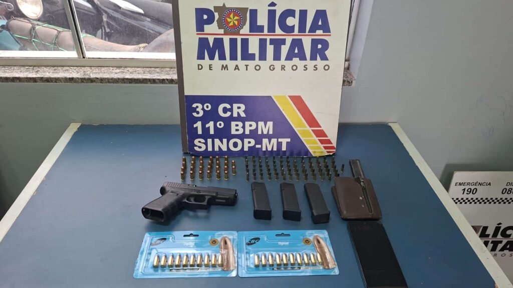 Pistola, carregadores e munições sobre mesa ao lado de identificação da Polícia Militar de Mato Grosso