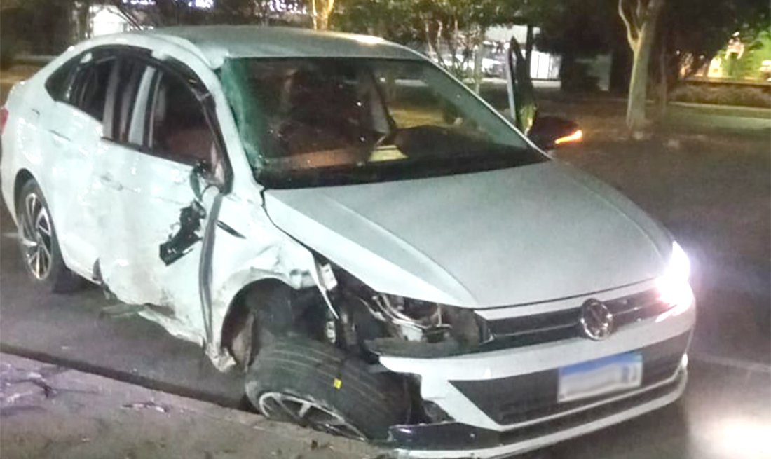 Carro branco com a lateral dianteira destruída, estacionado à noite em via pública